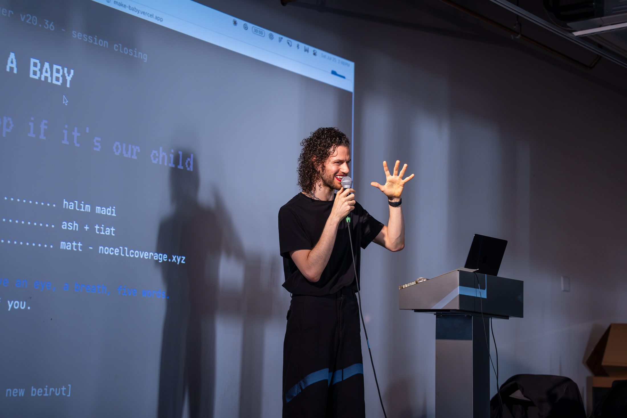 Halim raises a hand at the end of How to Make a Baby as the credits scroll on the projection behind him.