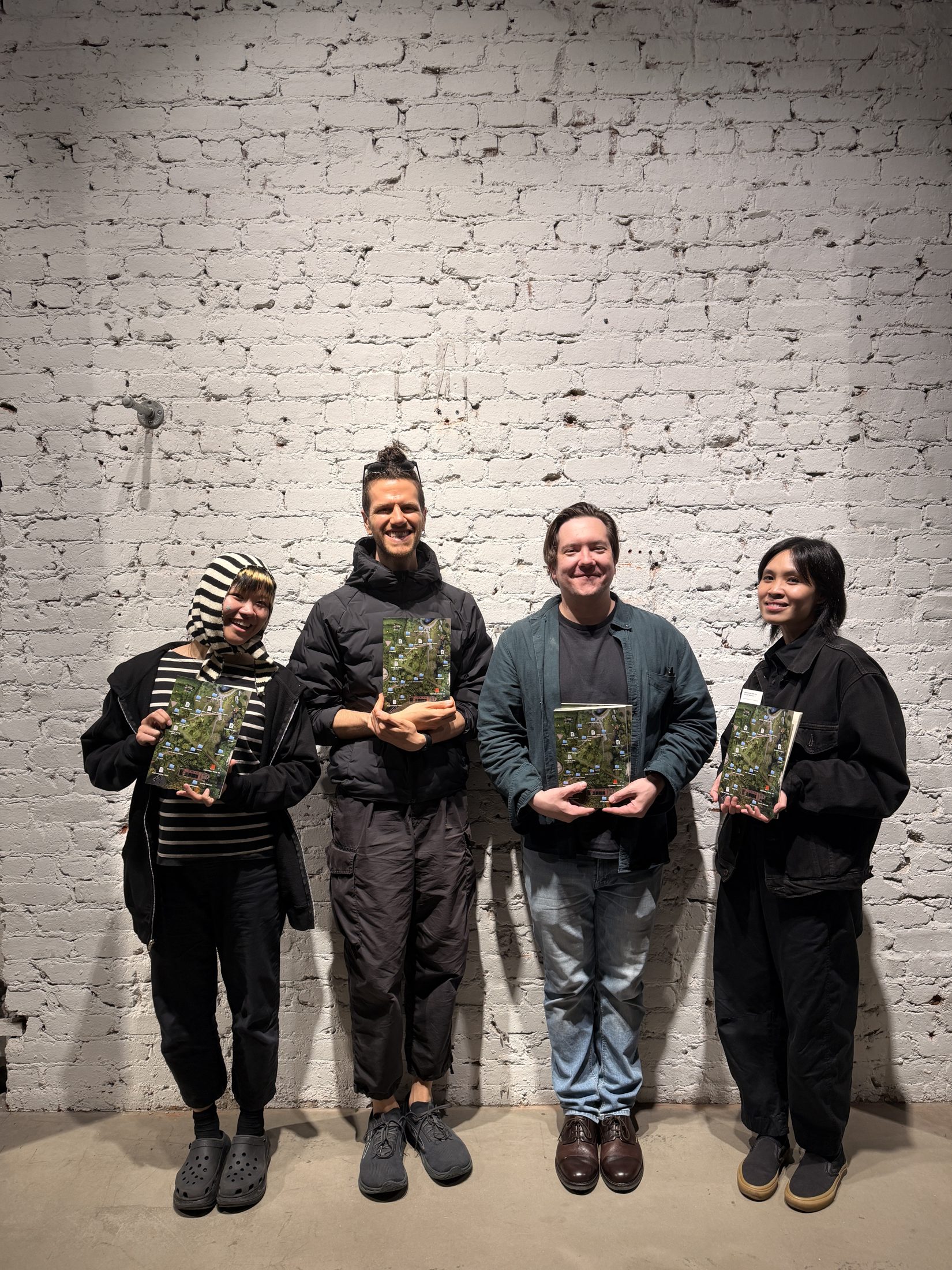 Halim and three fellow readers stand against a white brick wall at tiat, San Francisco, each holding the same book, after the sneak-peek reading on April 8, 2026.