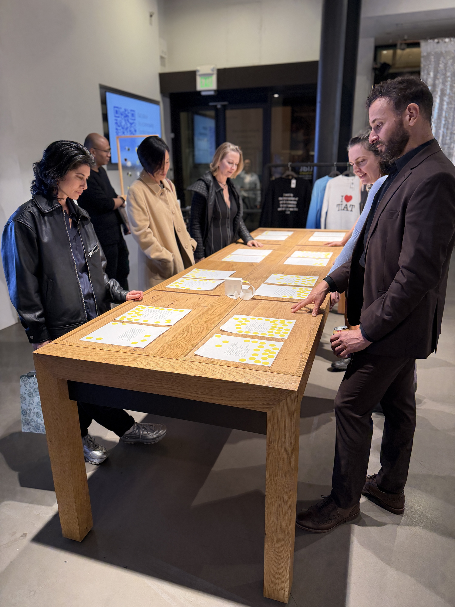 Poems with yellow voting dots spread across a wooden table at TIAT