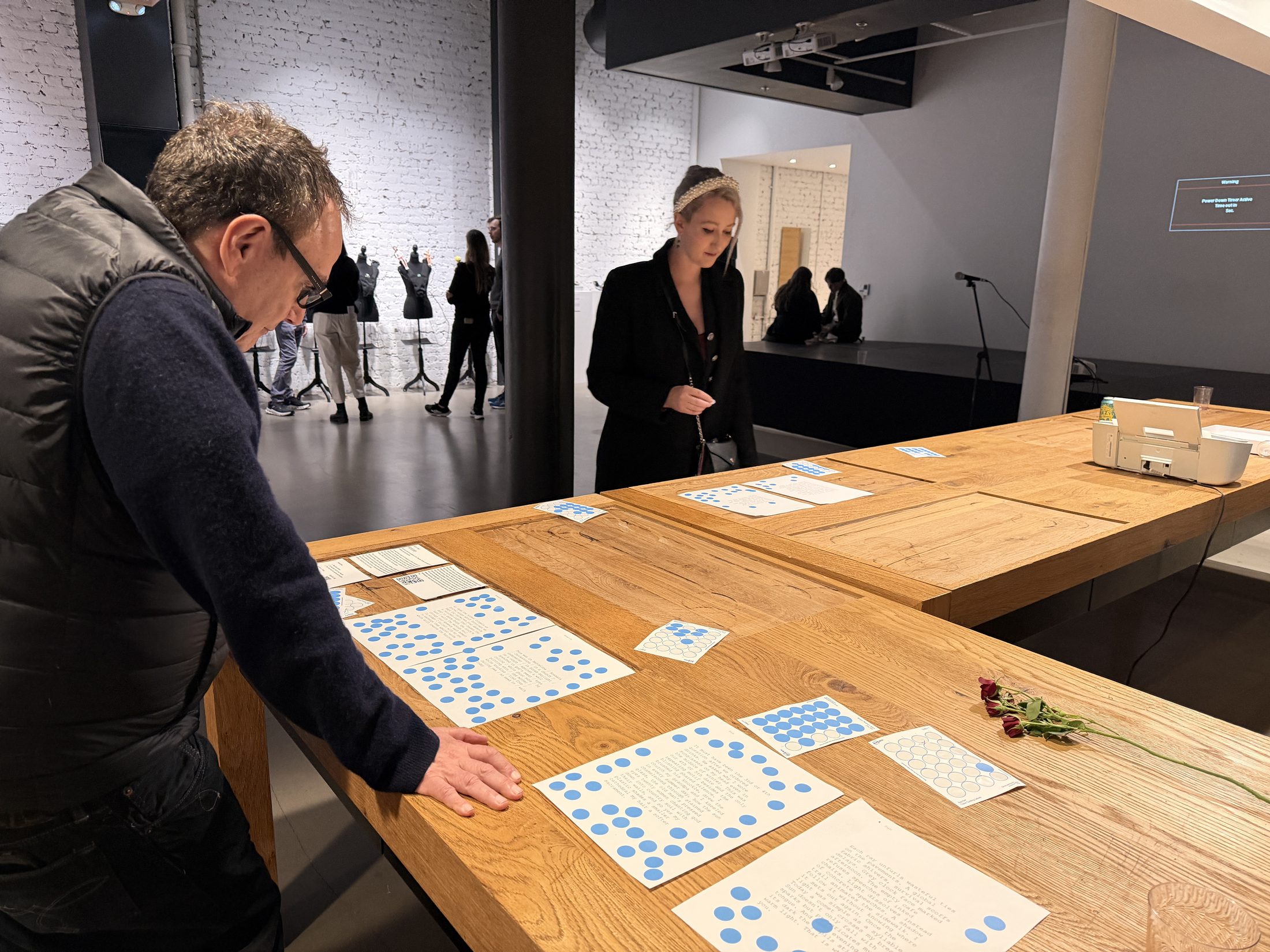 Audience examining printed poems with blue voting stickers at TIAT San Francisco