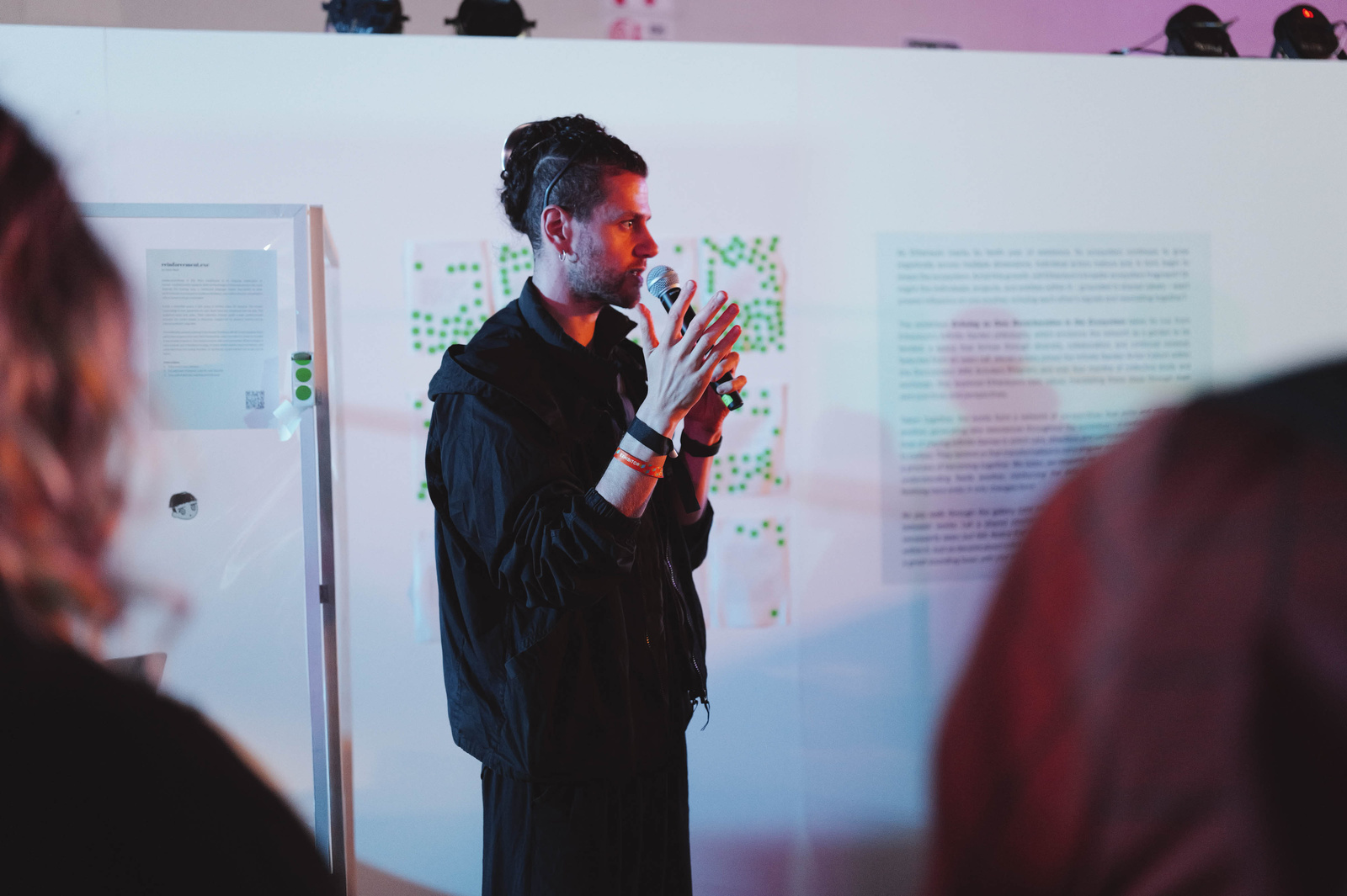 Halim explaining the piece beside a wall of printed poems covered in green voting dots
